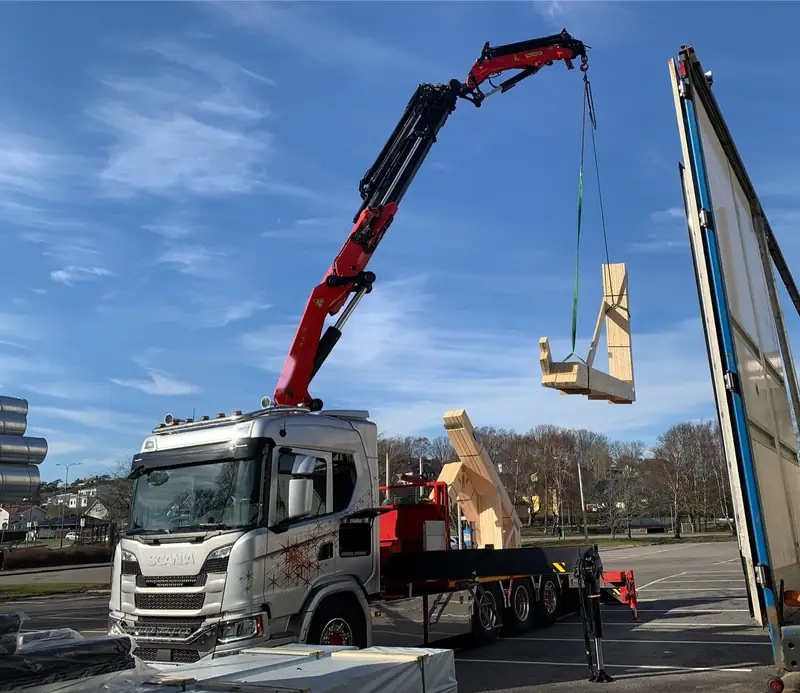 Caminhão Scania branco com guindaste içando um módulo de madeira sob céu azul