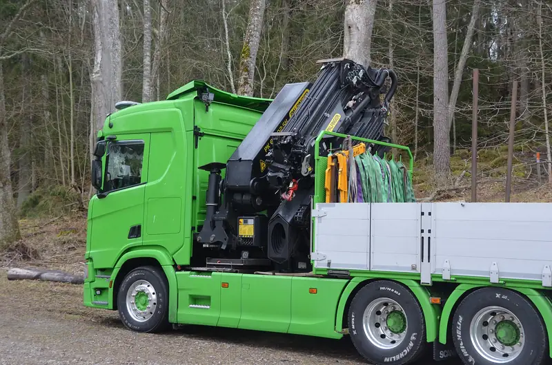 Caminhão verde com guindaste hidráulico Palfinger parado em estrada de floresta